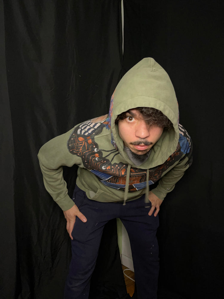 Latino model wearing green hoodie, hand painted showing solar panels in front, rockets in the back. Peacock feathers, mushrooms, earth, mars and the moon are painted.